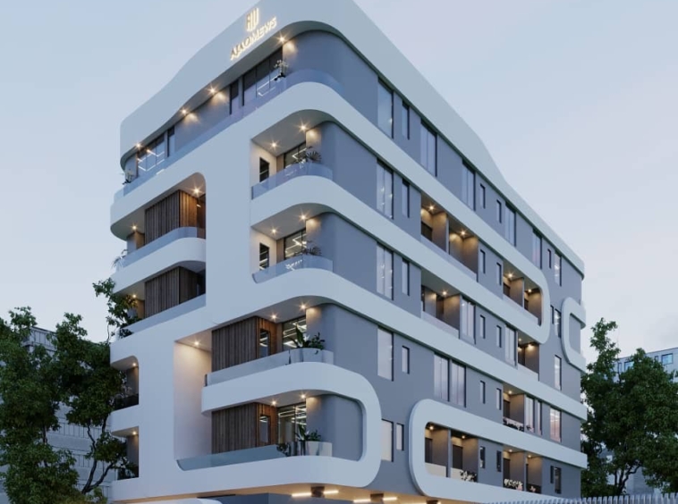 Modern multi-story residential building with rounded balconies and blue-gray exterior at dusk, with warm lights along the façade.