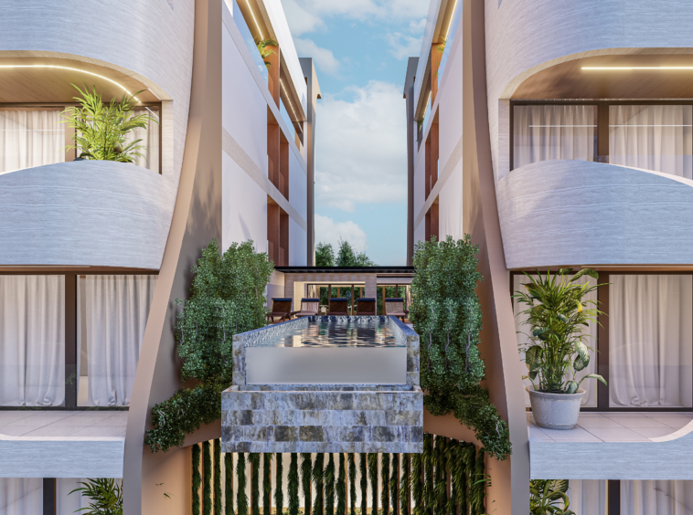 Symmetrical modern courtyard with a rectangular water fountain between two beige buildings, greenery along the sides and balconies above under a blue sky.