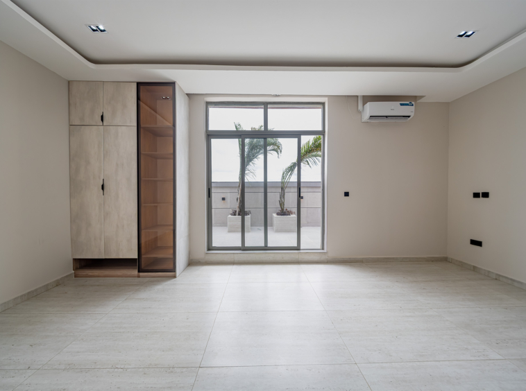 Bright empty room with a large glass sliding door to a patio and two potted palms outside; built-in cabinet on the left.