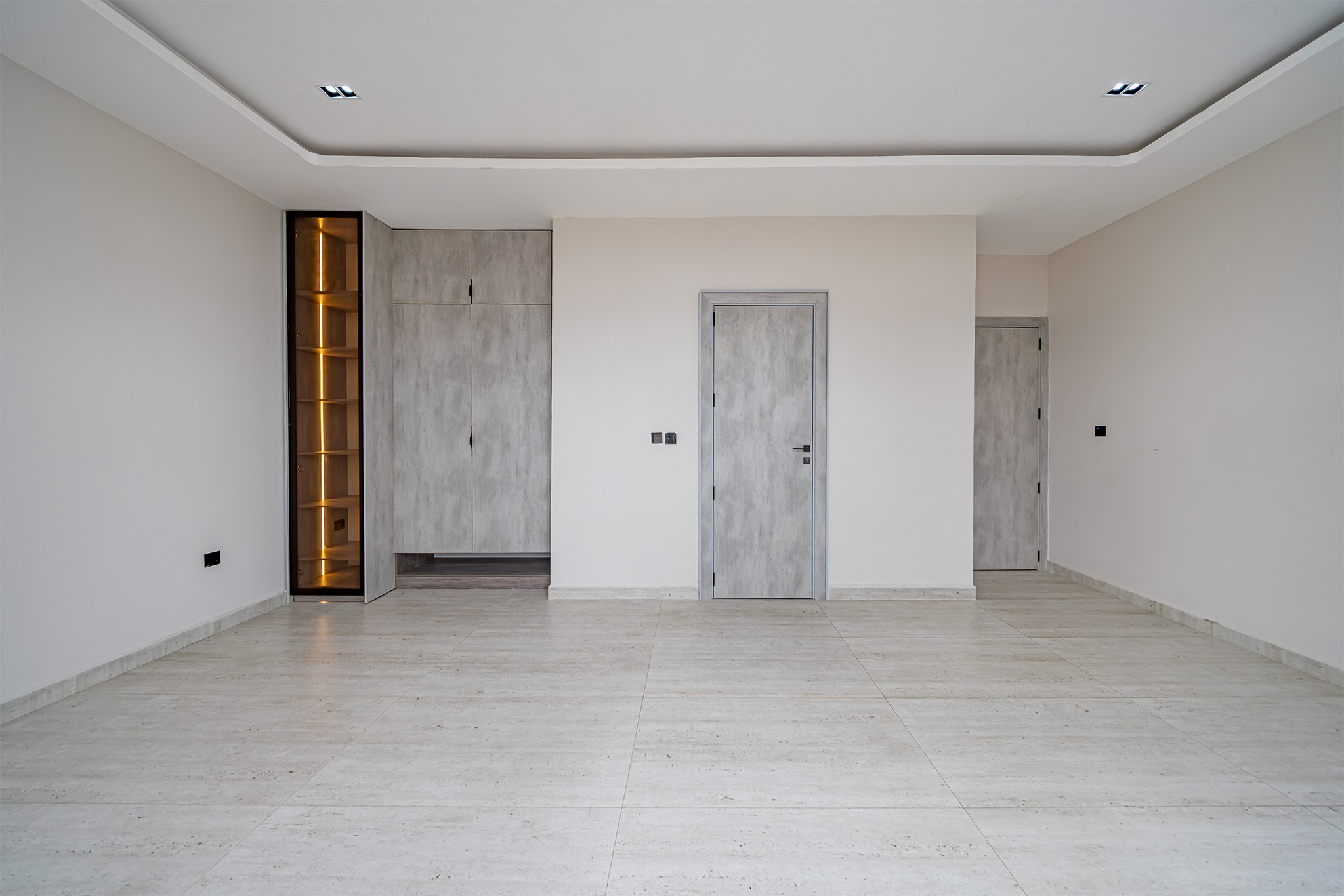 Empty modern room with light beige walls, light marble flooring, and gray built-in cabinets/doors.