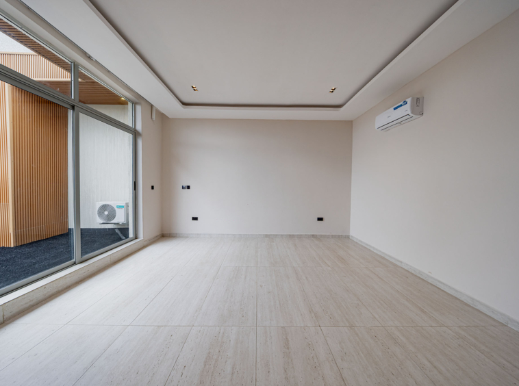 Empty modern room with large sliding glass doors to a balcony, white walls and ceiling, and a wall-mounted air conditioner on the right.