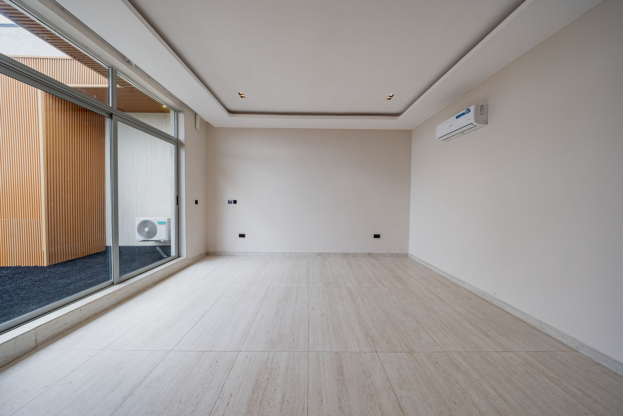 Empty modern room with large sliding glass doors to a balcony, white walls and ceiling, and a wall-mounted air conditioner on the right.