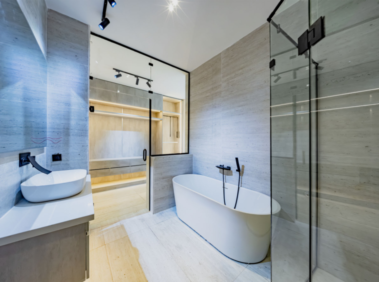 Modern bathroom with a white freestanding oval tub beside a glass shower enclosure and marble walls.
