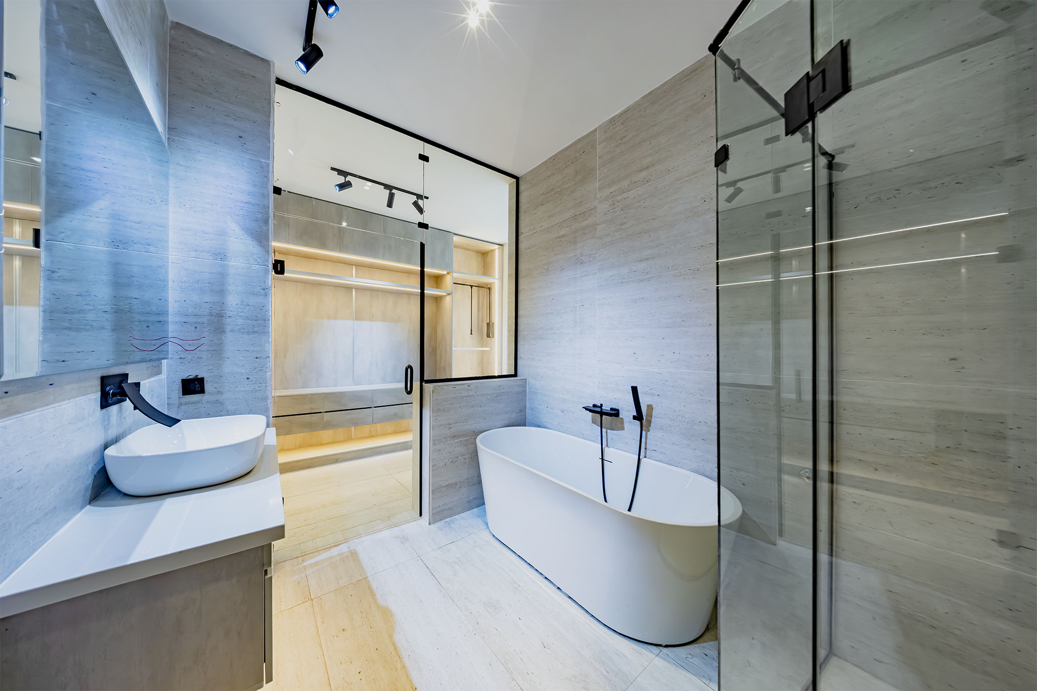 Modern bathroom with a white freestanding oval tub beside a glass shower enclosure and marble walls.