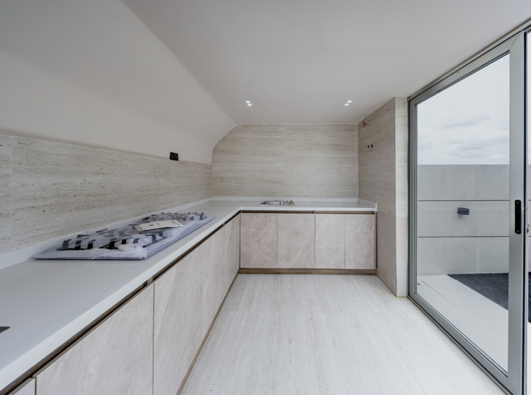 Modern kitchen with pale beige marble cabinets, white countertop, and a built-in gas stove along a long counter; large sliding glass door to the outdoors on the right side.