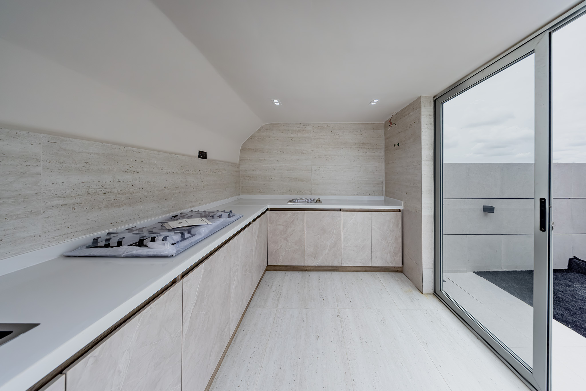 Modern kitchen with pale beige marble cabinets, white countertop, and a built-in gas stove along a long counter; large sliding glass door to the outdoors on the right side.