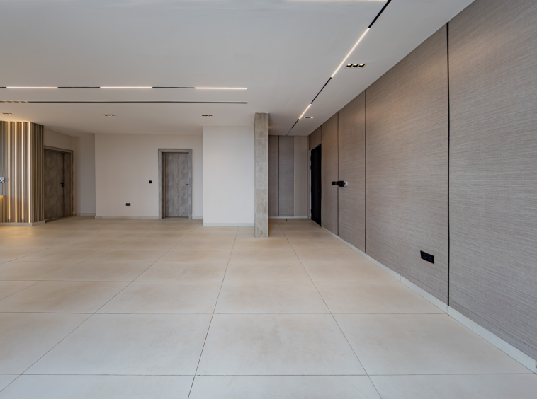 Modern lobby with large beige tile floor, right-side wood paneling, and elevator doors in the back.