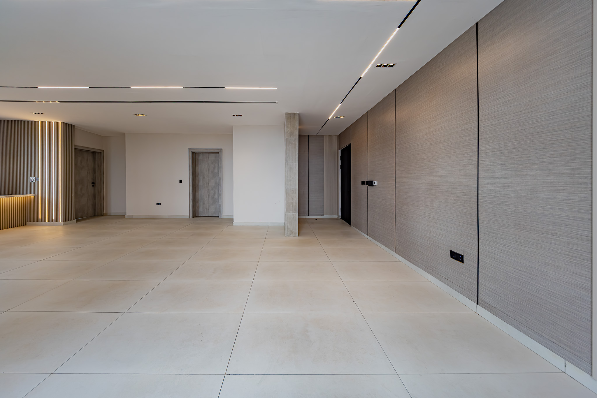 Modern lobby with large beige tile floor, right-side wood paneling, and elevator doors in the back.