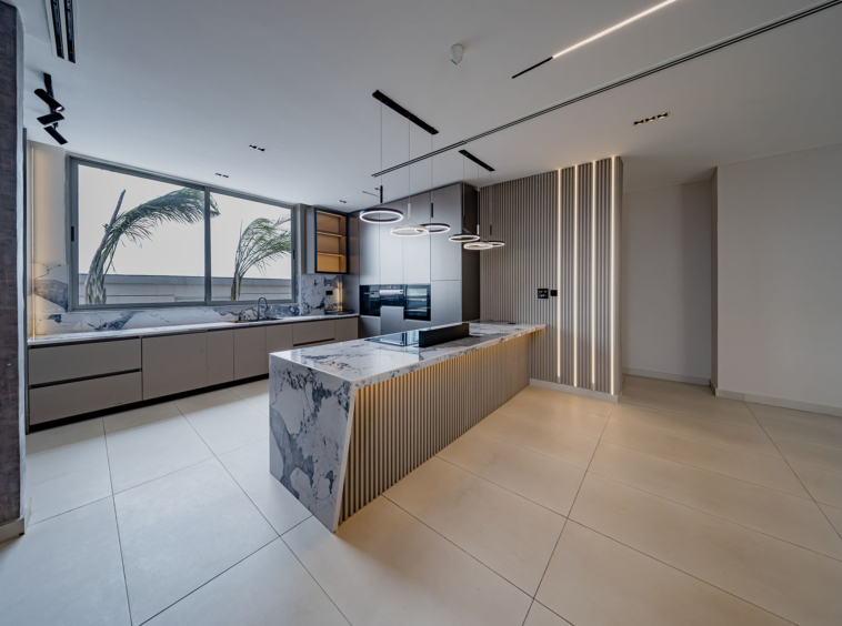 Modern kitchen with marble island, gray cabinetry, and circular pendant lights over the island.