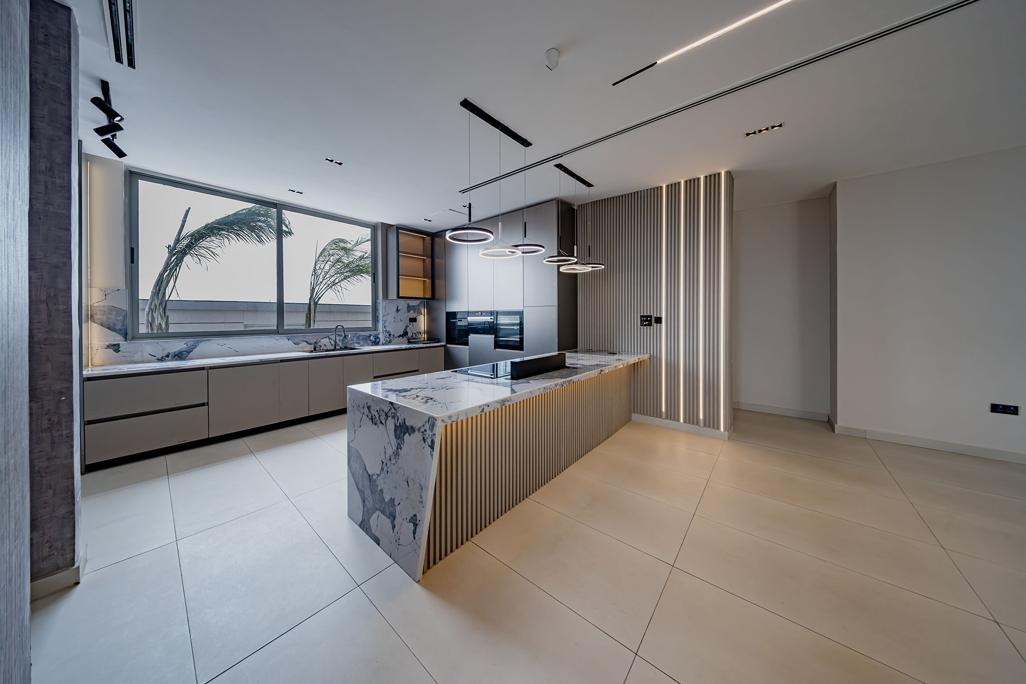 Modern kitchen with marble island, gray cabinetry, and circular pendant lights over the island.