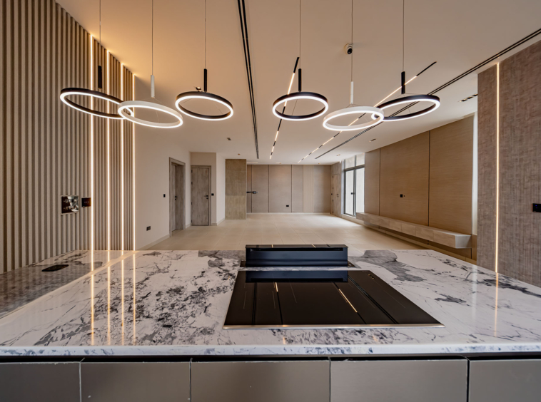 Modern reception area with circular halo pendant lights above a white marble countertop in a sleek lobby setting with wood paneling.