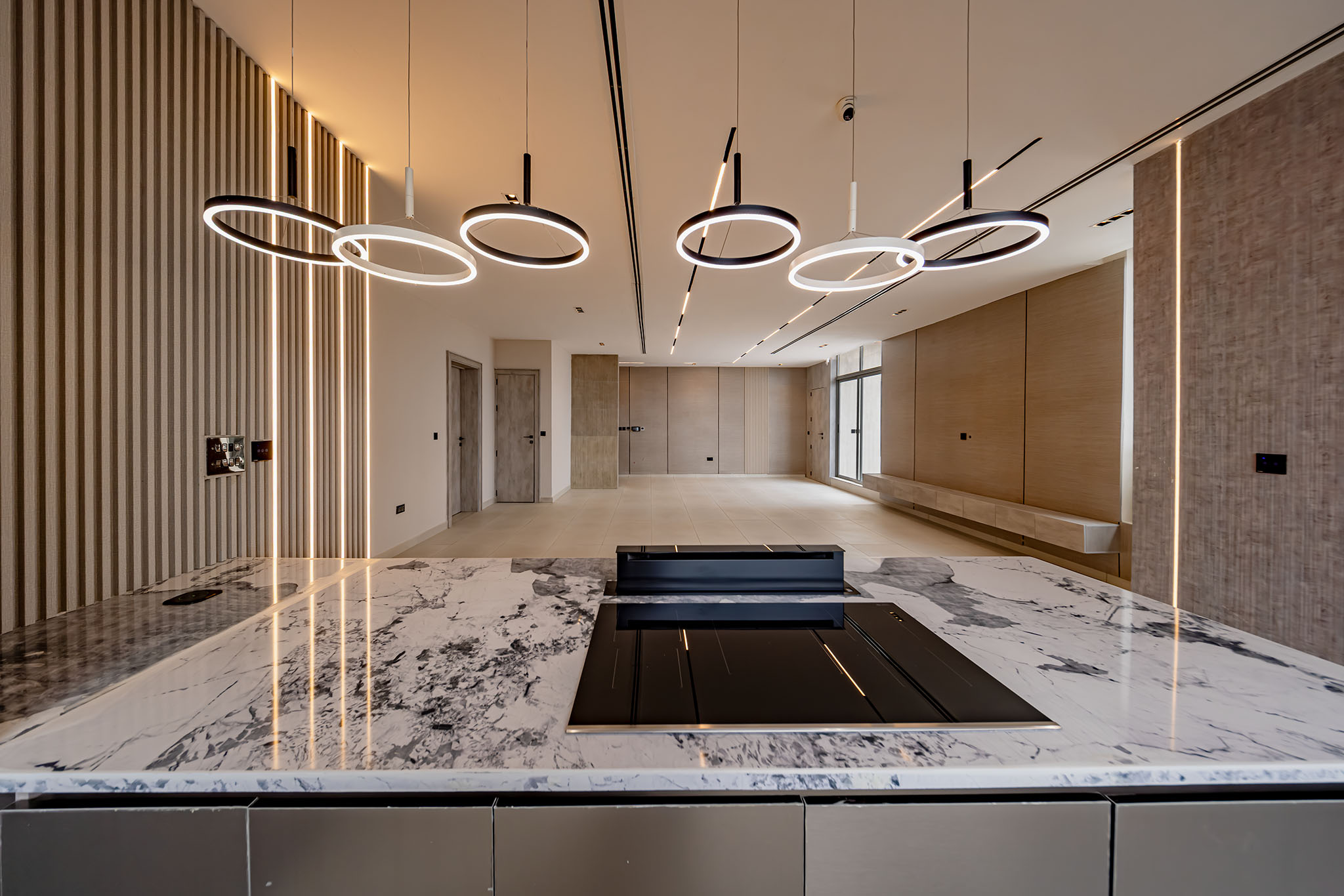 Modern reception area with circular halo pendant lights above a white marble countertop in a sleek lobby setting with wood paneling.